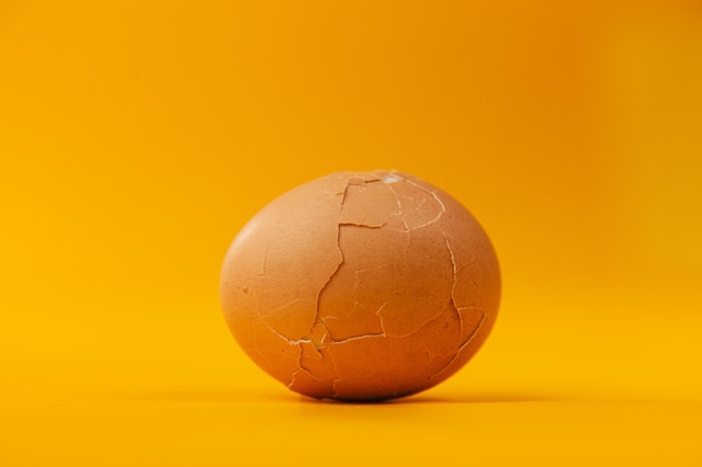 A brown egg, very cracked all over, sits in front of a golden background.