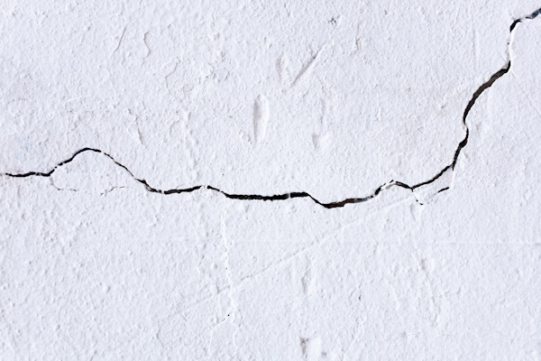 A gnarly black crack crosses from left to top right across a white textured wall.