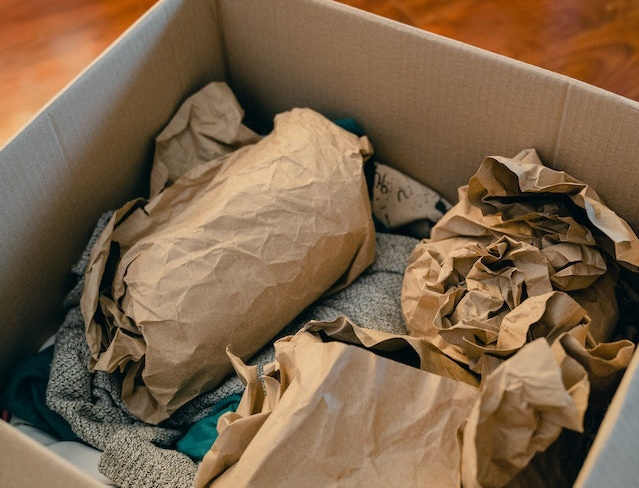 A box of clothes with crumpled brown packing paper on top.