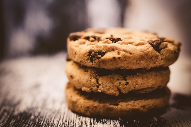 Close of of three stacked chocolate chip cookies against a blurred background of a wood grain weathered table.