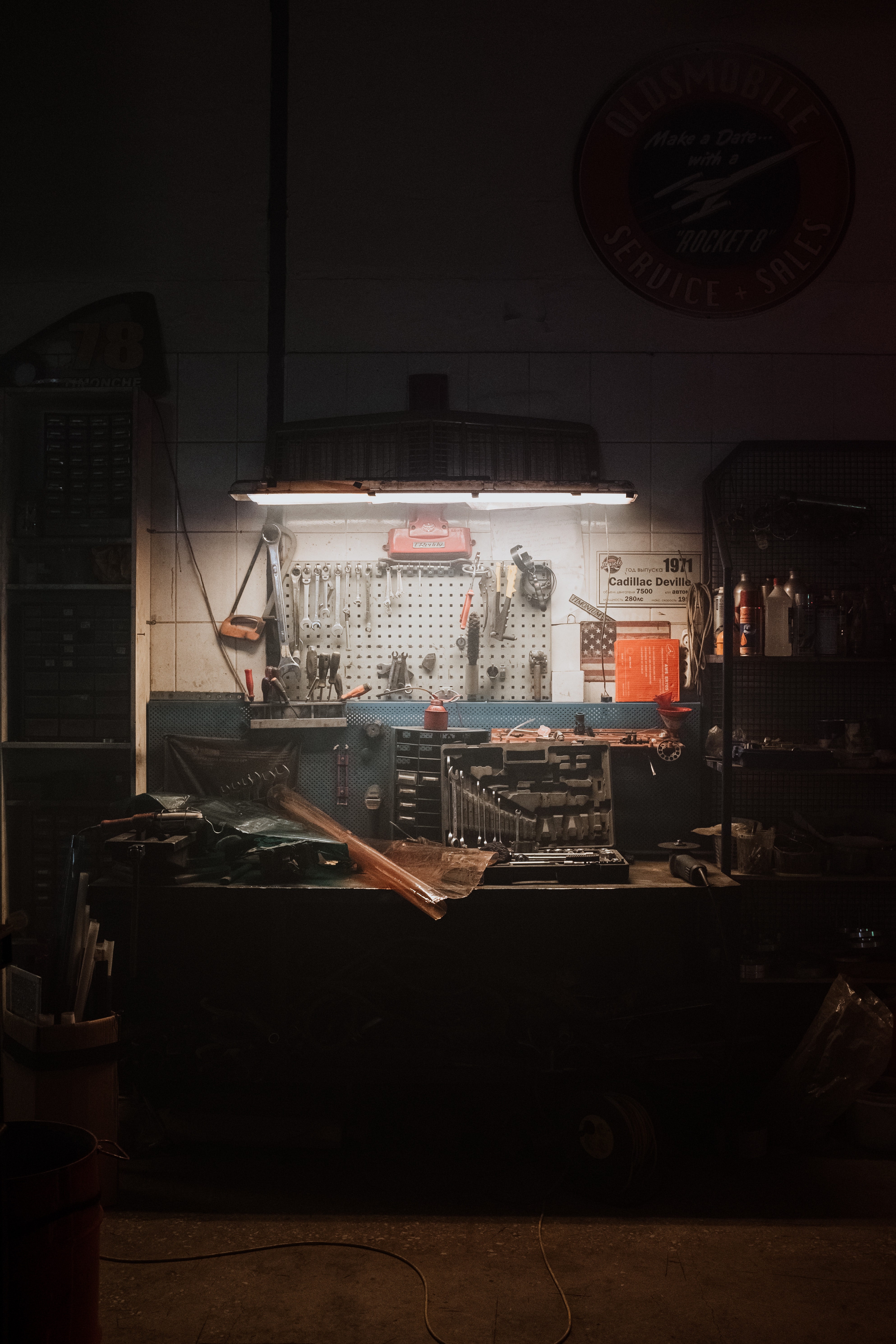An overhead light shines down on a garage work bench full of tools that spread up the wall on a pegboard.
